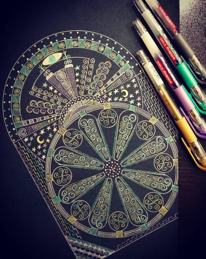 A sacred geometry composition part-finished on black paper, with gel pens beside it